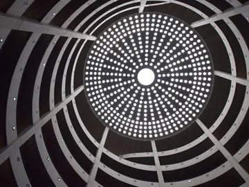 Runde Lichtinstallation leuchtet, umgeben von gebogenen Holzstrukturen.