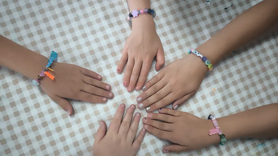Hände mit Armbändern auf kariertem Tuch.