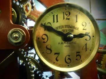Uhr zeigt Zeit, umgeben von Zahnrädern und mechanischen Teilen.