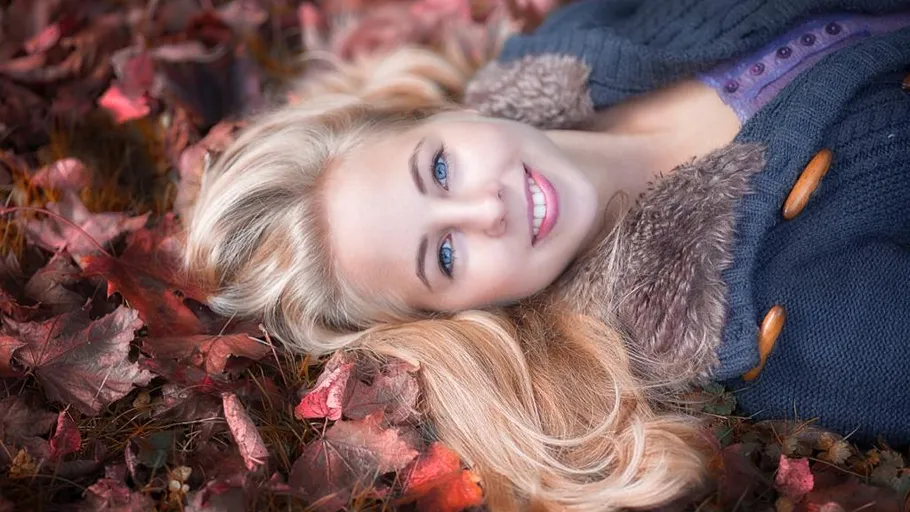 Woman lying on autumn leaves, smiling.