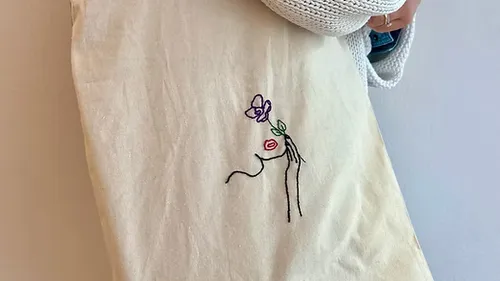 Embroidered tote bag with abstract face design.