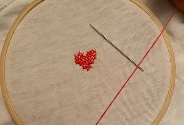 Embroidery hoop with red heart being stitched.