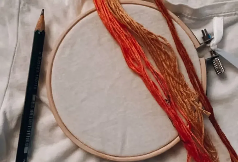 Stickrahmen mit Fäden und Bleistift daneben.