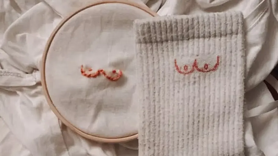 Embroidery with red thread on fabric and sock.