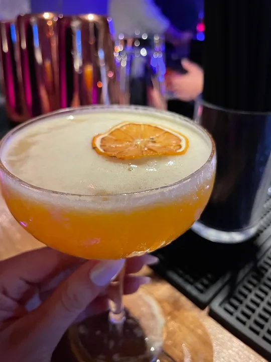 Cocktail mit getrockneter Orangenscheibe, Barhintergrund.