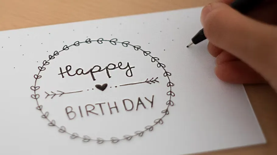 Hand decorates birthday card on table.