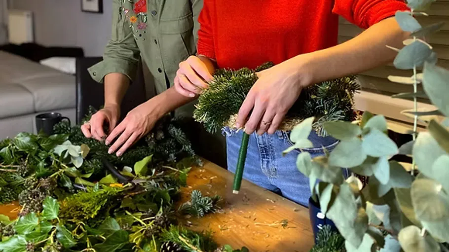 Two people making a wreath with greenery.