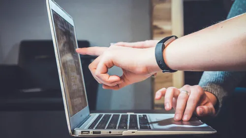 Hand zeigt auf Laptop-Bildschirm, Büro-Umgebung.