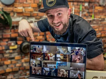 Ein Mann zeigt lächelnd auf einen Laptop mit Videoanrufen.