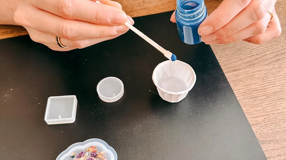 Hände mischen blaues Pulver mit Werkzeugen auf Tisch.