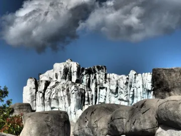 Eisberg erhebt sich majestätisch über steinigen Untergrund, wolkenverhangen.