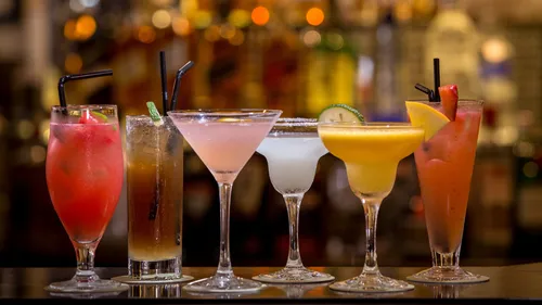 Bunte Cocktails auf einer Bartheke aufgereiht.