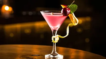 Pink cocktail with garnish on wooden table.