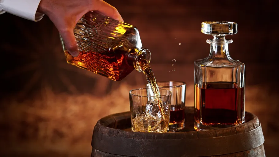 Hand gießt Whiskey in Glas auf Fass.