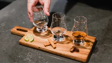 Hand placing glass on wooden board with drinks.