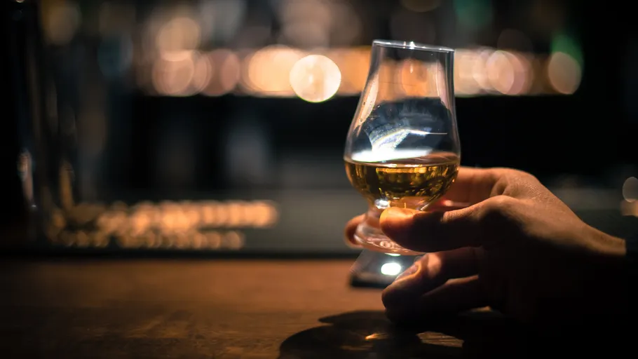 Glass of whiskey held by hand, bar background.