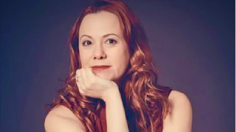 Woman posing with hand on chin, dark background.