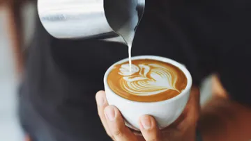 Person pours milk into latte art coffee.