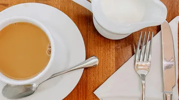 Coffee cup, cutlery, and milk on wooden table.