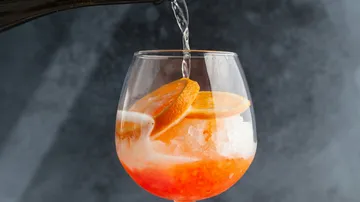 Drink being poured into glass with oranges.