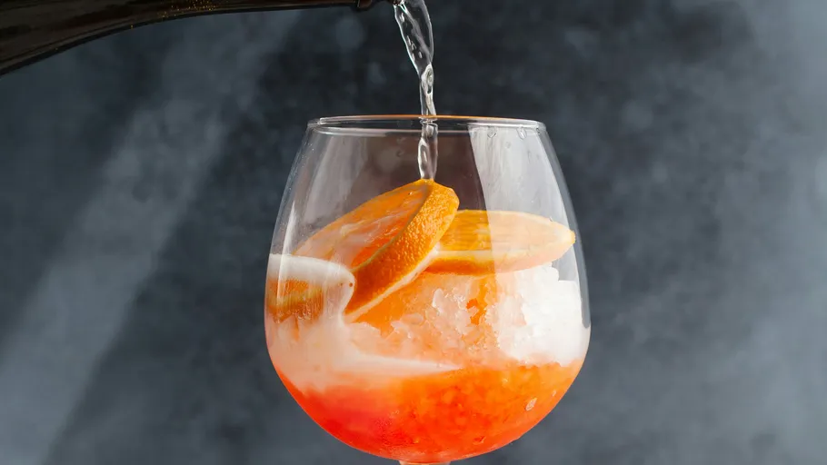 Drink being poured into glass with oranges.