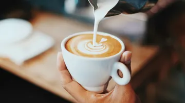 Barista pouring milk into coffee cup.