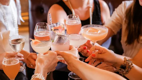 Hands holding cocktails in a group toast.