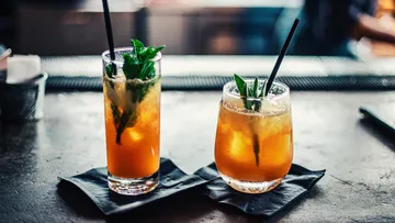 Two cocktails with straws on a bar.