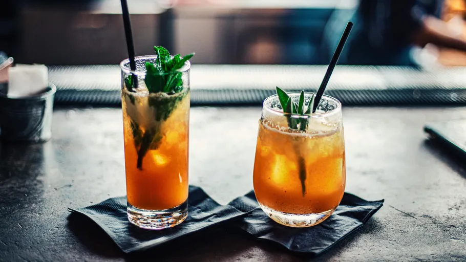 Zwei Cocktails mit Strohhalmen an einer Bar.