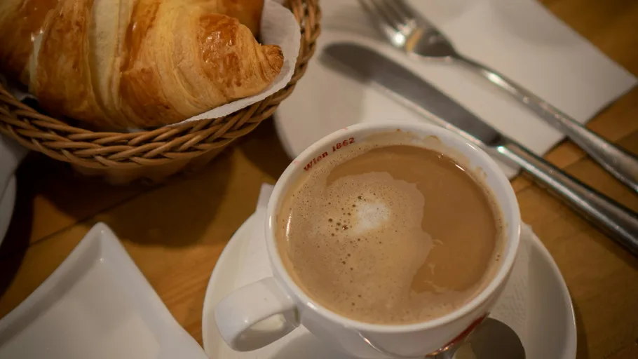 Kaffee und Croissant auf Holztisch.