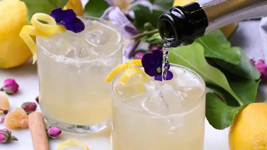 Zwei Cocktails mit Zitronengarnitur und Blumen.