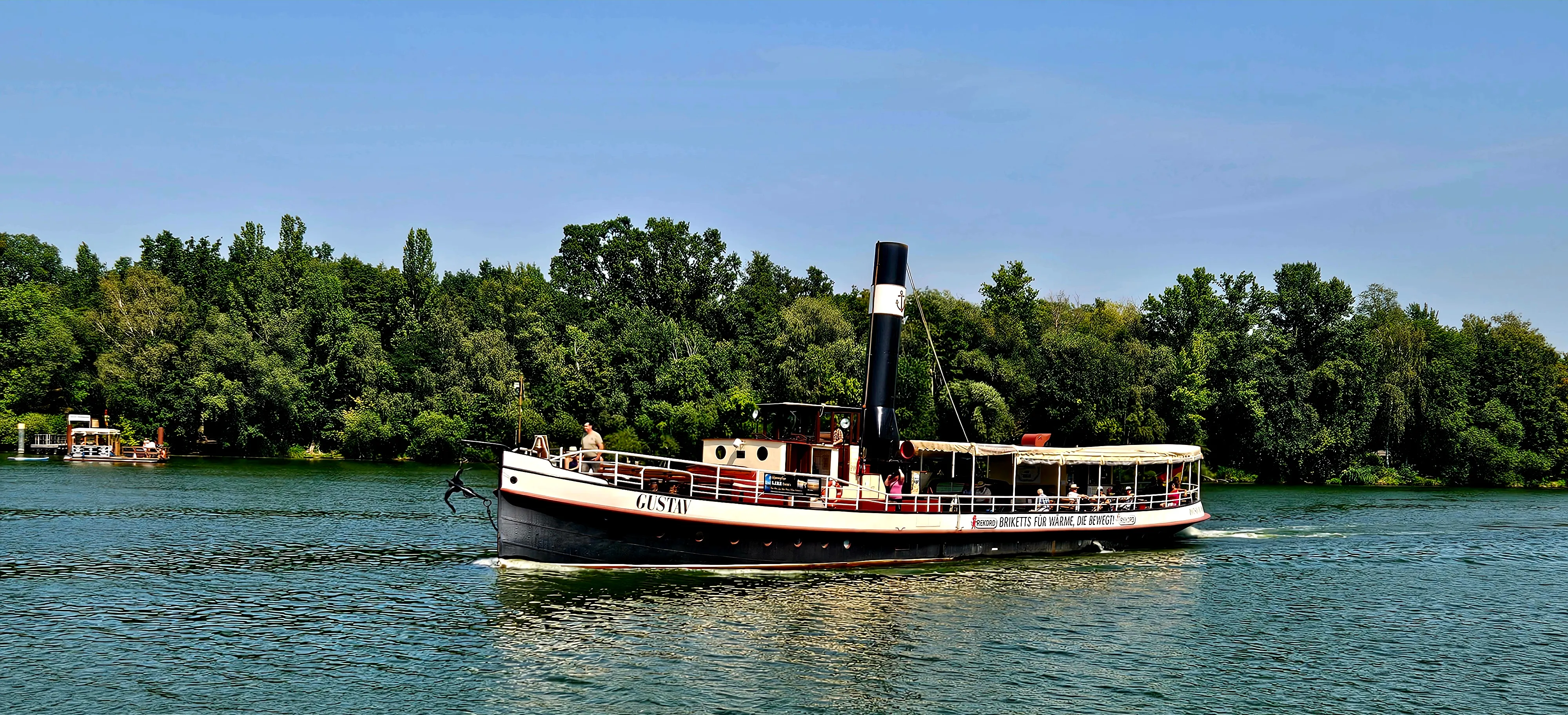 Historic steamship cruising on a river, forest background.