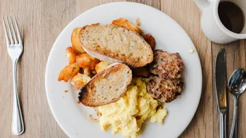 Frühstücksteller mit Eiern, Toast, Wurst und Kartoffeln.