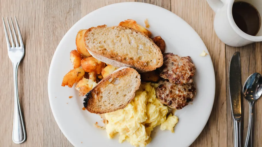 Breakfast plate with eggs, toast, sausage, and potatoes.