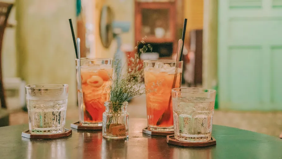 Four drinks and a vase on table.