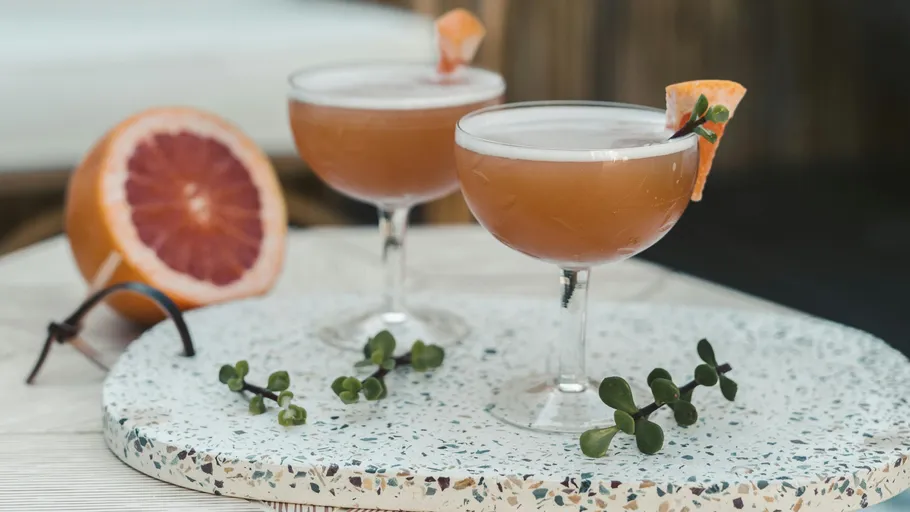 Two cocktails with grapefruit garnish on table.