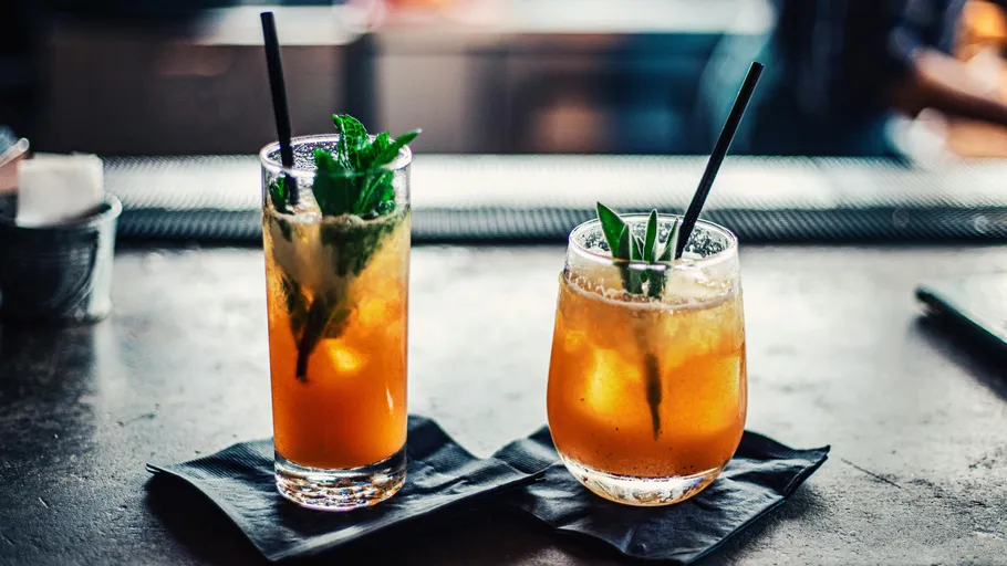 Two cocktails on black napkins at bar.