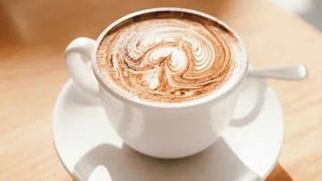 Latte mit Herzmuster-Schaum auf Tisch.