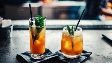 Two cocktails with straws on a bar.