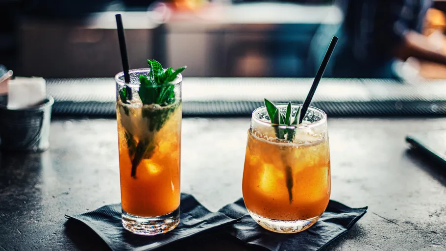 Two cocktails with straws on a bar.