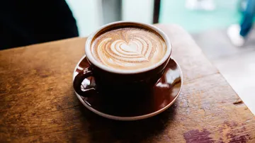 Coffee cup with heart latte art on table.
