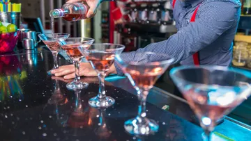 Barkeeper gießt Getränke in Martinigläser.