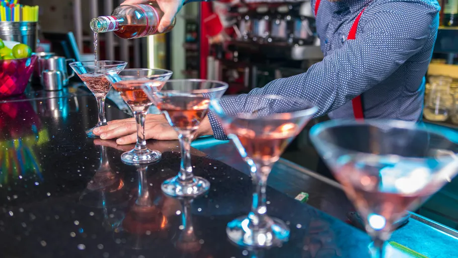 Barkeeper gießt Getränke in Martinigläser.
