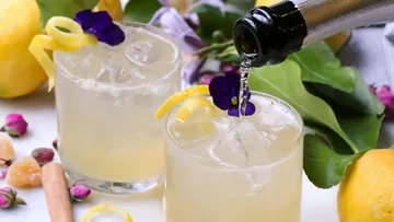 Cocktails with lemon and flowers on table.