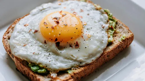 Fried egg on avocado toast, white plate.