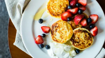 Cheese pancakes with berries and cream on plate.