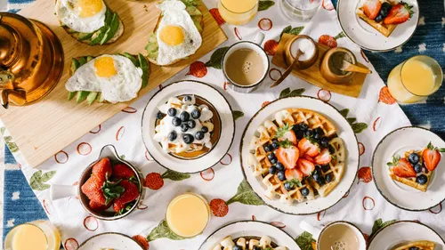 Breakfast with waffles, egg, avocado, fruits, and drinks.