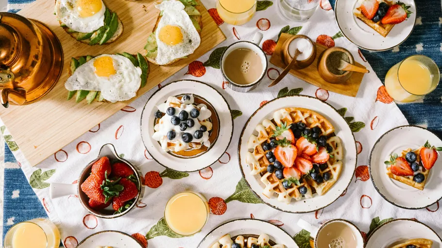 Frühstück mit Waffeln, Ei, Avocado, Früchten, und Getränken.
