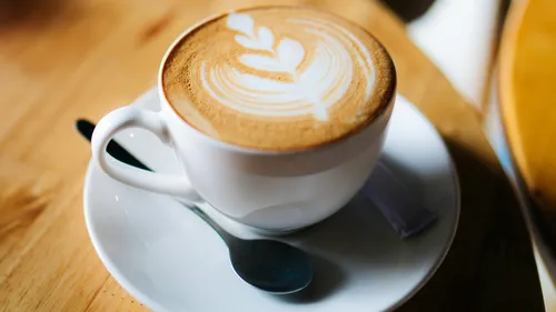 Latte with art in white cup, table setting.