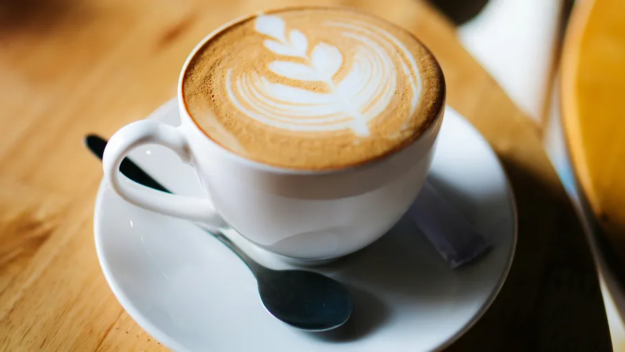 Latte with art in white cup, table setting.